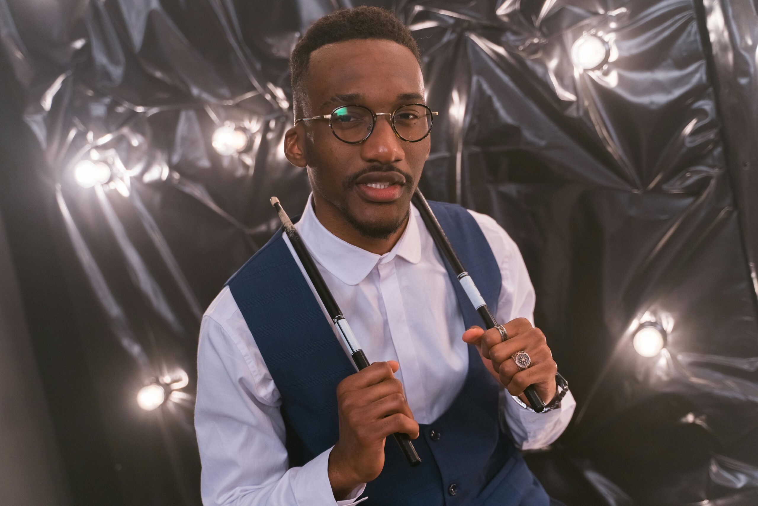 Close-up of a stylish drummer posing with drumsticks in front of a lighted backdrop.